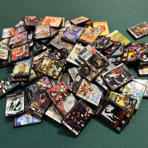 May include: A collection of miniature PlayStation 2 game cases, featuring various game titles. The cases display colorful artwork and game titles, including "Killzone" and "Max Payne". The cases are scattered, creating a visually engaging display.