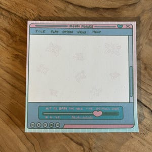 Puede incluir: Un bloc de notas azul claro y rosa con un diseño de pantalla de ordenador. La pantalla tiene un fondo blanco con un diseño de mariposa rosa claro. La parte inferior de la pantalla tiene un reproductor de música azul y verde con el texto "HIT ME BABY ONE MORE TIME - BRITANIA SPARS" y un corazón rosa.