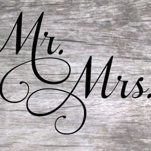 May include: Black and white calligraphy script with the words "Mr. Mrs." on a wood background.