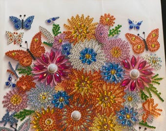 May include: A framed artwork featuring a colorful beaded flower bouquet with butterflies. The flowers are made of various colored beads, including orange, yellow, pink, blue, and red. The butterflies are also beaded and have blue, orange, and white wings.