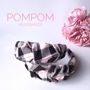 May include: Two fabric headbands with a black and white check pattern, one on top of the other. The headbands have a knotted design. The text "POMPOM HEADBANDS" is in pink above them. Pink flowers are in the background.