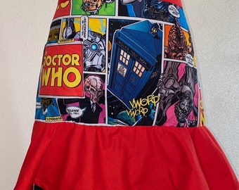 Może przedstawiać: Czerwony fartuch z nadrukiem komiksowym przedstawiającym TARDIS Doktora Who, Daleków i innych postaci. Fartuch ma falbankę u dołu.
