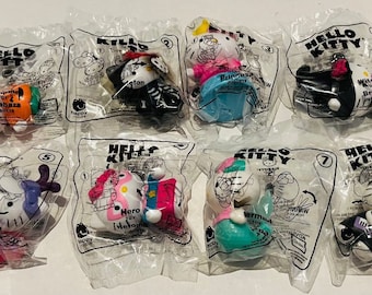 Może przedstawiać: Kolekcja ośmiu zabawek Hello Kitty w zapieczętowanych plastikowych opakowaniach. Każda zabawka to inna postać, w tym motyl, księżniczka i syrena. Opakowanie zawiera logo Hello Kitty i nazwy postaci.