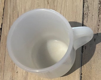 Może przedstawiać: Biały ceramiczny kubek o zaokrąglonym korpusie i zakrzywionym uchwycie. Kubek jest pusty i wydaje się czysty. Kubek stoi na drewnianej powierzchni.