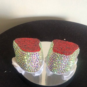 Puede incluir: Un par de zapatos de beb&eacute; decorados con pedrer&iacute;a iridiscente y ribete rojo.