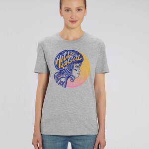 K&ouml;nnte beinhalten: Graues T-Shirt mit einem Grafikdruck einer Frau mit Helm und dem Text "Hit Like a Girl" in einem blau-orangenen Farbschema.