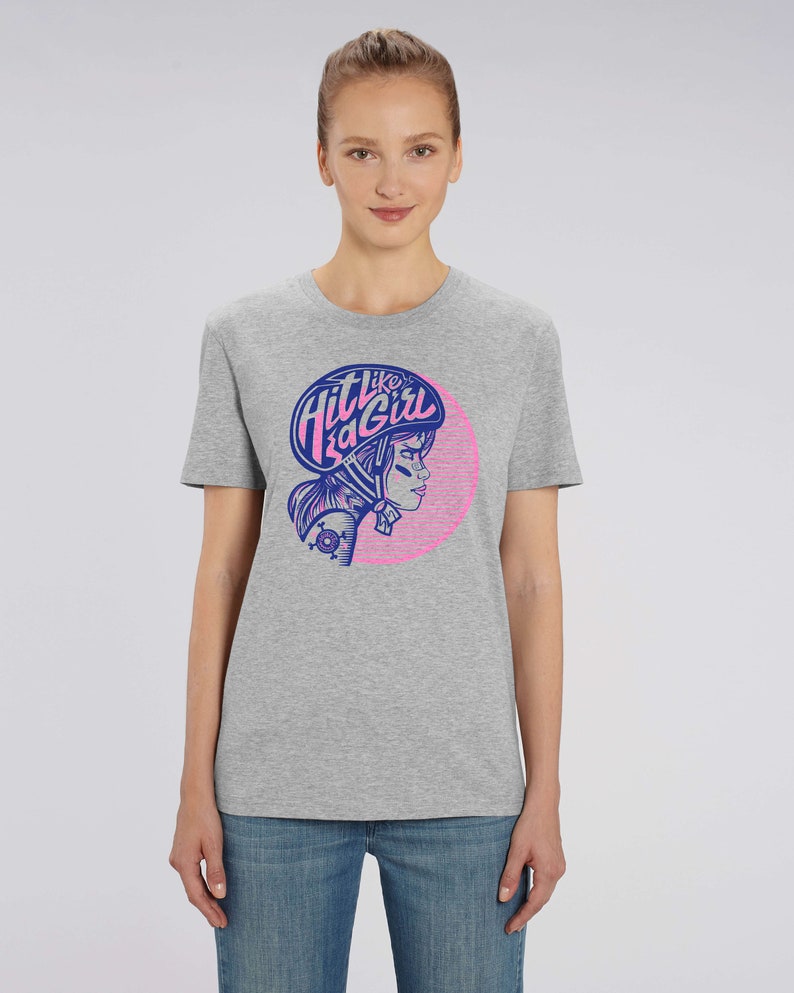 K&ouml;nnte beinhalten: Graues T-Shirt mit einer pinkfarbenen und blauen Grafik einer Frau mit Helm und dem Text "Hit like a girl".