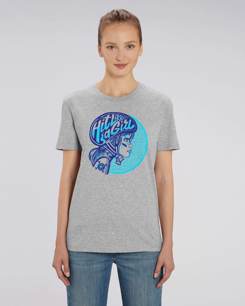 K&ouml;nnte beinhalten: Graues T-Shirt mit einem blauen und wei&szlig;en Grafikdruck einer Frau mit Helm und dem Text "Hit like a Girl".