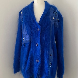 May include: A blue fluffy cardigan with floral embellishments and button closure.