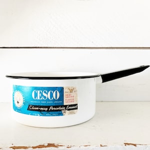 May include: White enamel saucepan with a black handle and rim. The pan features a blue and white label with the text "CESCO" and "Clean-easy Porcelain Enamel". A vintage kitchenware item.