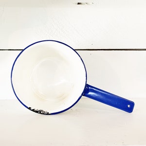 以下が含まれることがあります： 青い縁取りと取っ手のある白いエナメル製のピッチャー。ピッチャーは使い古されたビンテージな外観です。