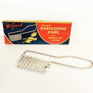 May include: Vintage Hi-Speed Vegetable Garnishing Knife and French Fry Cutter in its original box. The box is red, blue, and yellow with the product name and instructions printed on it. The knife is made of metal and has a wavy blade.