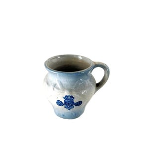 May include: A small, light blue and white ceramic pitcher with a handle. The pitcher has a decorative blue floral design on the front. The interior of the pitcher is a darker gray color.