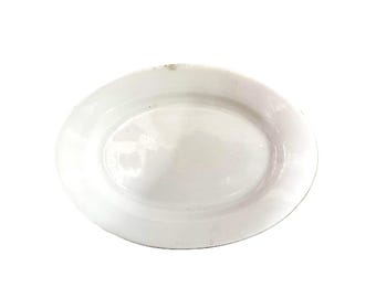 May include: A plain white oval ceramic platter with a smooth, glossy finish and a slightly raised rim. The dish features a simple, clean design with no patterns or decorations, presenting a uniform white surface throughout the entire piece.