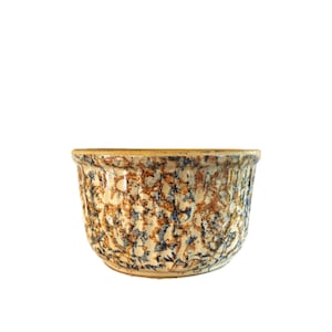 May include: A ceramic bowl featuring a textured exterior with a mottled pattern of cream, tan, brown, and dark blue speckles. The bowl has a wide, open top and a rounded base, showcasing a consistent, dense, and organic colour distribution throughout.