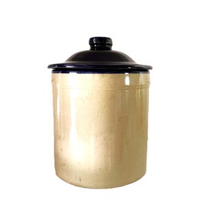 May include: A cylindrical stoneware crock with a smooth, light beige finish and a glossy, dark navy blue lid. The lid features a small, rounded knob at the center. The container has a straight-sided body with a subtle horizontal ridge near the top.