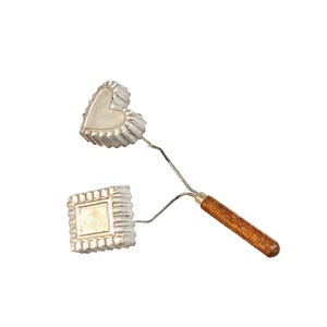 May include: A dual-headed kitchen tool featuring a silver-toned heart-shaped mold and a square-shaped mold with fluted edges. Both metal molds are attached to thin wire stems that converge into a single cylindrical wooden handle with a brown finish.