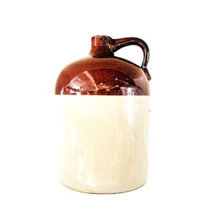 Pode incluir: Uma jarra cilíndrica de cerâmica com um esmalte de dois tons. A parte superior, incluindo o pescoço e a alça, tem um acabamento em castanho escuro brilhante, enquanto o corpo inferior é de uma cor creme clara e lisa. Possui uma alça lateral.
