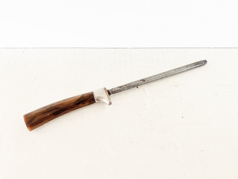 May include: A vintage metal knife sharpener with a brown wooden handle. The sharpener is made of metal and has a wooden handle.