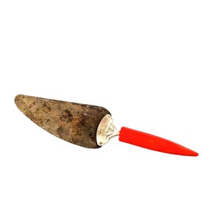 Może przedstawiać: Zabytkowy serwer do ciasta z matowym, teksturowanym ostrzem i jasnoczerwonym uchwytem. Ostrze ma stonowany brązowy kolor, a uchwyt jest żywo czerwony. Serwer ma srebrny metalowy akcent.