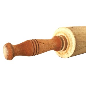 May include: A wooden rolling pin with a light brown barrel and a darker brown handle. The handle has a rounded end and is attached to the barrel with a circular joint. The rolling pin is designed for kitchen use.