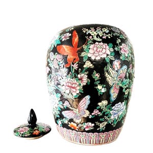 May include: Black ceramic jar with a lid, featuring a colorful floral and butterfly design. The jar has a rounded shape and a decorative base with a patterned border. The lid is black with a floral design.