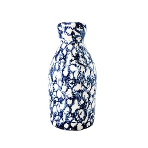 Puede incluir: Un jarrón de cerámica con base blanca y un patrón de manchas azules. El jarrón tiene un cuello estrecho y un cuerpo redondeado. El diseño recuerda a un patrón moteado.