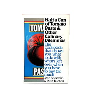 May include: A hardcover cookbook titled Half a Can of Tomato Paste & Other Culinary Dilemmas by Jean Anderson & Ruth Buchan. The cover features a graphic illustration of a blue tomato paste can with a red tomato and black text on white.