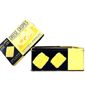 Puede incluir: Dos cajas vintage de Holland Cheese Crispies. Las cajas son rectangulares con una combinación de colores azul marino y amarillo. El texto "Cheese Crispies" y "Holland Che-Cri" es visible. Las cajas contienen crujientes de queso.