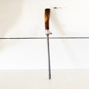 May include: A vintage steel knife sharpener with a brown and white plastic handle.