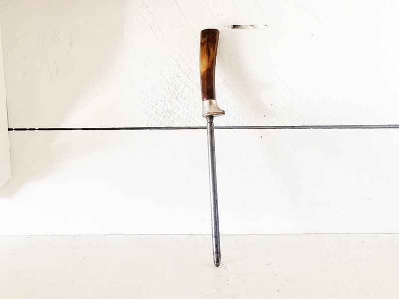 May include: A vintage steel knife sharpener with a brown and white plastic handle.