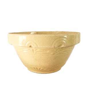 May include: A light yellow ceramic mixing bowl with a wide rim and a rounded body. The bowl features embossed decorative patterns around the rim and on the body. The bowl is set against a white background.