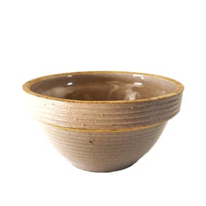 May include: A beige ceramic bowl with a wide, rounded shape. The bowl has a textured, ridged exterior and a smooth, light brown interior. The rim is a darker shade of brown.