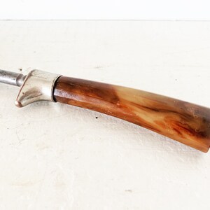 May include: A vintage metal and brown plastic steak knife with a silver handle.
