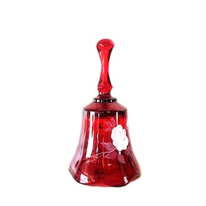 Puede incluir: Una campana de cristal rojo rubí translúcido con un diseño floral grabado y transparente en el lateral. La campana presenta un mango alto y delgado, junto con una base acampanada de borde festoneado, mostrando un tono carmesí profundo en todo.