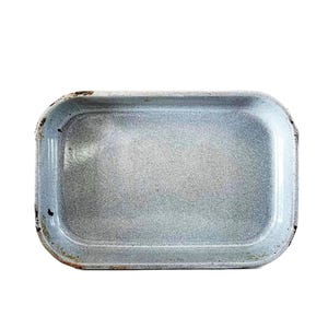 Puede incluir: Una bandeja rectangular de esmalte azul claro con esquinas redondeadas. La bandeja presenta signos de desgaste en los bordes, lo que sugiere edad o uso. La superficie interior tiene una textura sutil y moteada.