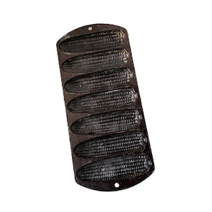 May include: A cast iron cornbread pan with six corn cob-shaped molds. The pan is dark gray and has a textured surface, perfect for baking. The pan is designed to make individual corn-shaped cornbreads.