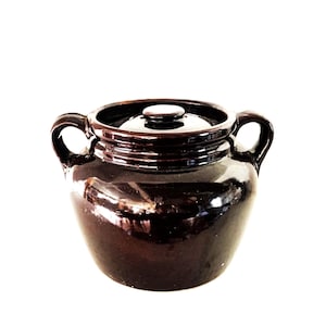 May include: A dark brown ceramic crock with a lid and two handles. The crock has a glossy finish and a classic, vintage design. Perfect for kitchen decor or storage.