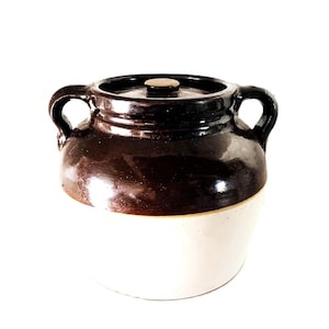 Peut inclure: Un pot en céramique bicolore avec un couvercle. La partie supérieure est brun foncé brillant, tandis que la moitié inférieure est blanc crème. Il a deux poignées arquées et un petit bouton en bois sur le couvercle.