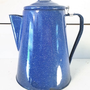 Puede incluir: Una cafetera de esmalte azul con un acabado moteado y un asa plateada. La cafetera tiene una tapa con una pequeña asa plateada.