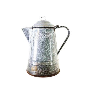 May include: Vintage enamelware coffee pot with a speckled gray and white pattern. The pot has a lid, spout, and a black metal handle. The base of the pot has a brown, aged appearance. A classic kitchenware item.