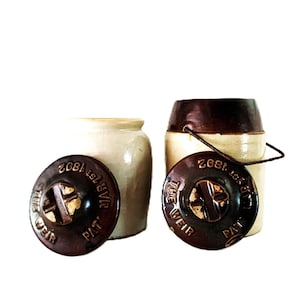 Può includere: Due antichi vasi in gres con coperchi marrone scuro. Uno è color crema, l'altro ha la parte superiore marrone scuro e un manico in filo di ferro. I coperchi sono impressi con la scritta "THE WEIR PAT. MAR 1ST 1892."