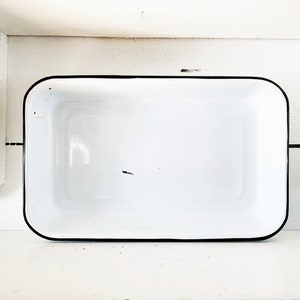 May include: White enamel baking dish with a black rim. The dish is empty and has a slight discoloration on the bottom.