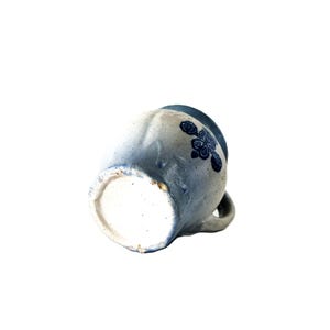 May include: A handmade ceramic mug with a blue floral design. The mug has a light blue and white speckled finish, with a small handle and a slightly flared rim. The floral design is a darker shade of blue.
