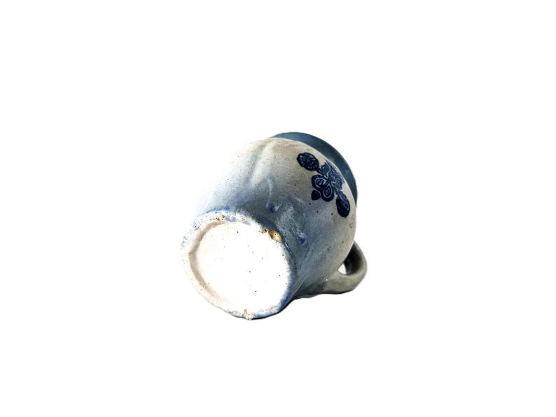 May include: A handmade ceramic mug with a blue floral design. The mug has a light blue and white speckled finish, with a small handle and a slightly flared rim. The floral design is a darker shade of blue.