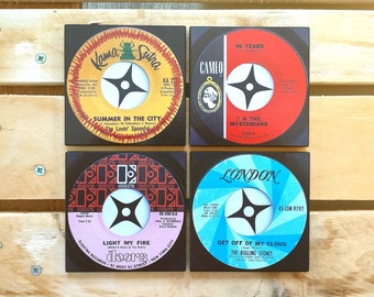Puede incluir: Cuatro posavasos cuadrados con etiquetas de discos de vinilo de 45 RPM vintage. Las etiquetas incluyen "Kama Sutra", "96 Tears", "Light My Fire" y "Get Off of My Cloud". Cada posavasos tiene un borde negro.