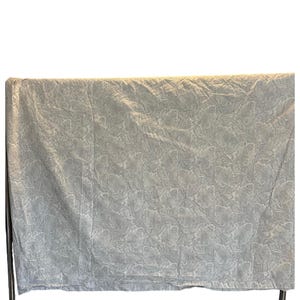 May include: A pale blue fabric with a floral pattern, displayed on a black metal rack. The fabric has a textured surface and a subtle design. The colour is a muted, light blue, suitable for bedding or home decor.