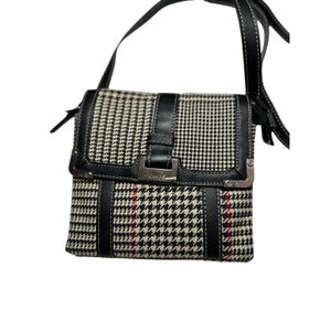 Puede incluir: Bolso bandolera con estampado de pata de gallo en blanco y negro con correa y detalles en cuero negro. El bolso tiene un cierre de solapa con hebilla plateada y la marca "CHAPS" es visible. Rayas rojas acentúan el patrón.