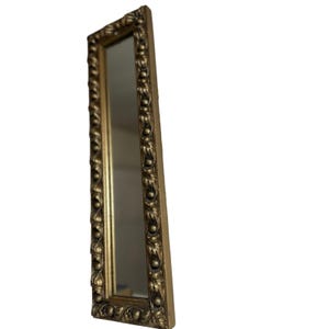 May include: A tall, rectangular wall mirror featuring a metallic gold frame with a repeating decorative pattern of raised spheres and curved leaf-like motifs along the entire border, surrounding a clear, reflective glass center panel.