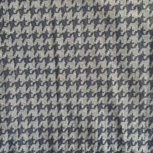 May include: A close-up of a fabric with a houndstooth pattern. The design features a repeating pattern of dark blue and light grey shapes, creating a textured appearance. This textile is suitable for various apparel and home decor projects.